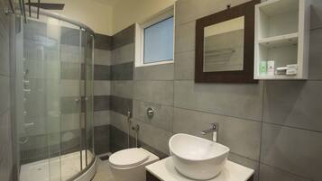 A modern bathroom with a glass-enclosed shower, a white sink, and a small window.