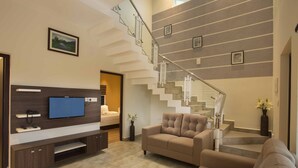 A modern living room with a flat-screen TV, a sofa, a staircase, and a dining area. - Foggy Knolls Resort (Meenachil)