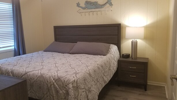 A neatly made bed with a patterned bedspread, a dark wooden headboard, and a bedside table with a lamp and a small electronic device.