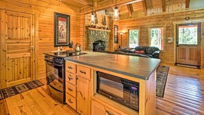 Interior de una cabaña de troncos con cocina que cuenta con una chimenea de piedra, armarios de madera y electrodomésticos modernos.