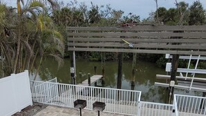 A patio area with a picnic table and benches, a white fence, and a view of a water body with a dock. - Water Views, Pool, Private boat dock, Walking distance to Times Square (Fort Myers Beach)