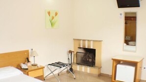 Hotelkamer met een bed, een kleine tafel met lamp, een stoel, een open haard, een aan de muur bevestigde televisie, en een bloemen schilderij.