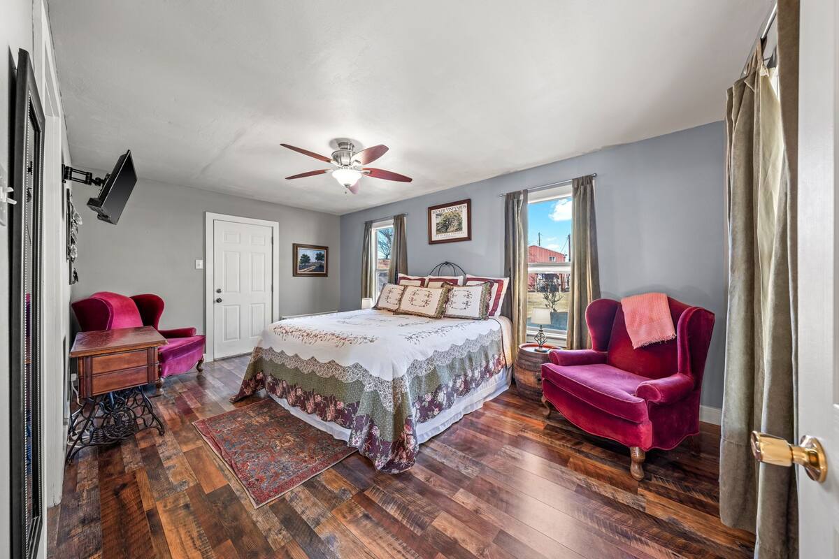 A bedroom with a bed, a desk, a chair, a ceiling fan, and a window.