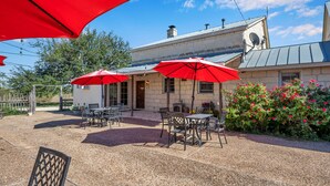 Une terrasse extérieure avec des tables et des chaises, des parasols rouges et, au fond, un bâtiment en pierre surmonté d’un toit en métal.