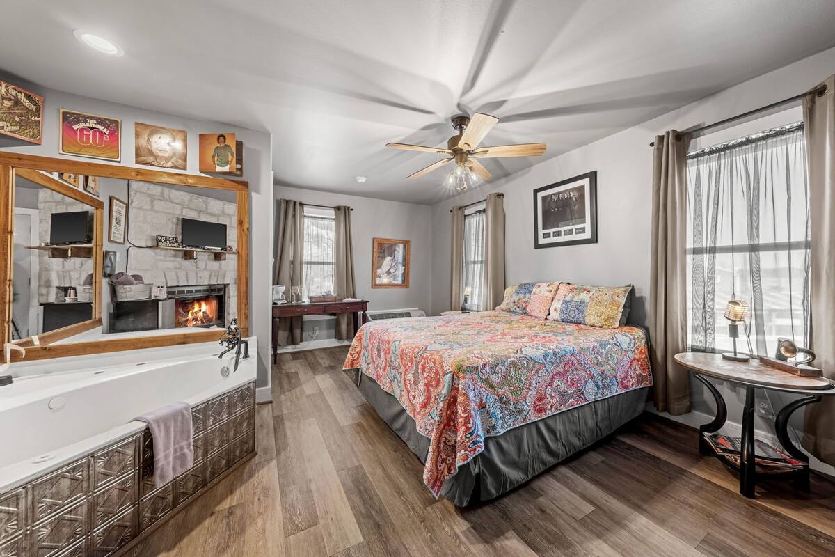 A bedroom with a large bed, a bathtub, a ceiling fan, and a fireplace.