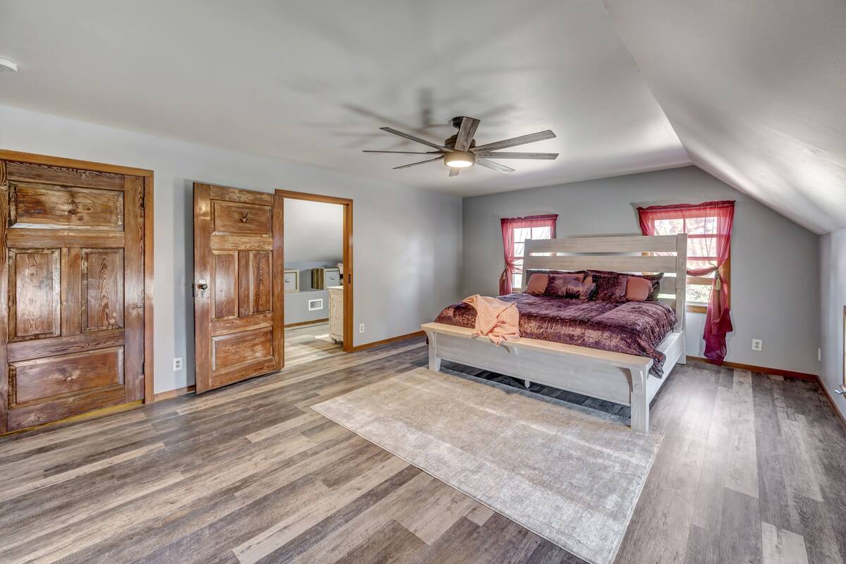 A bedroom with a wooden bed, a ceiling fan, and a large window with red curtains.