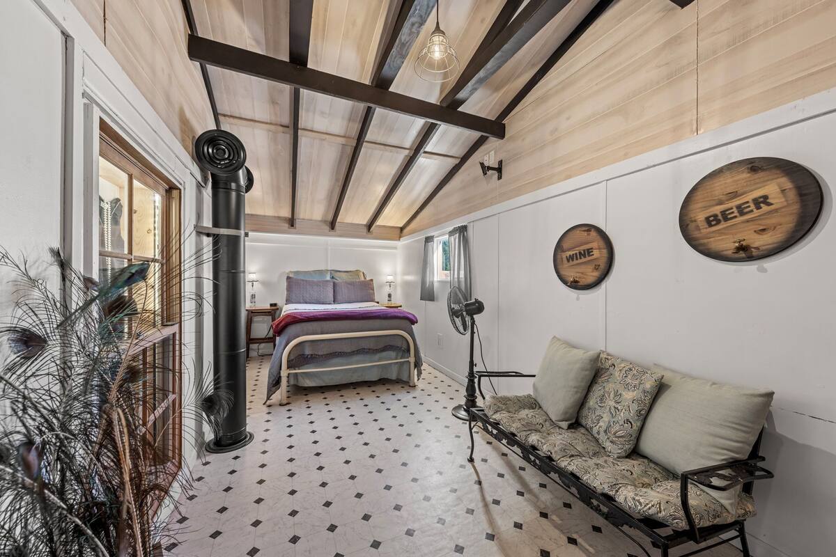 A bedroom with a bed, a sofa, a fan, and a wall with wooden signs labeled 'BEER' and 'WINE'.