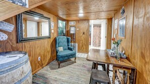 Une pièce aux murs en bois, avec un grand miroir, un fauteuil bleu, une table en bois et un tonneau.
