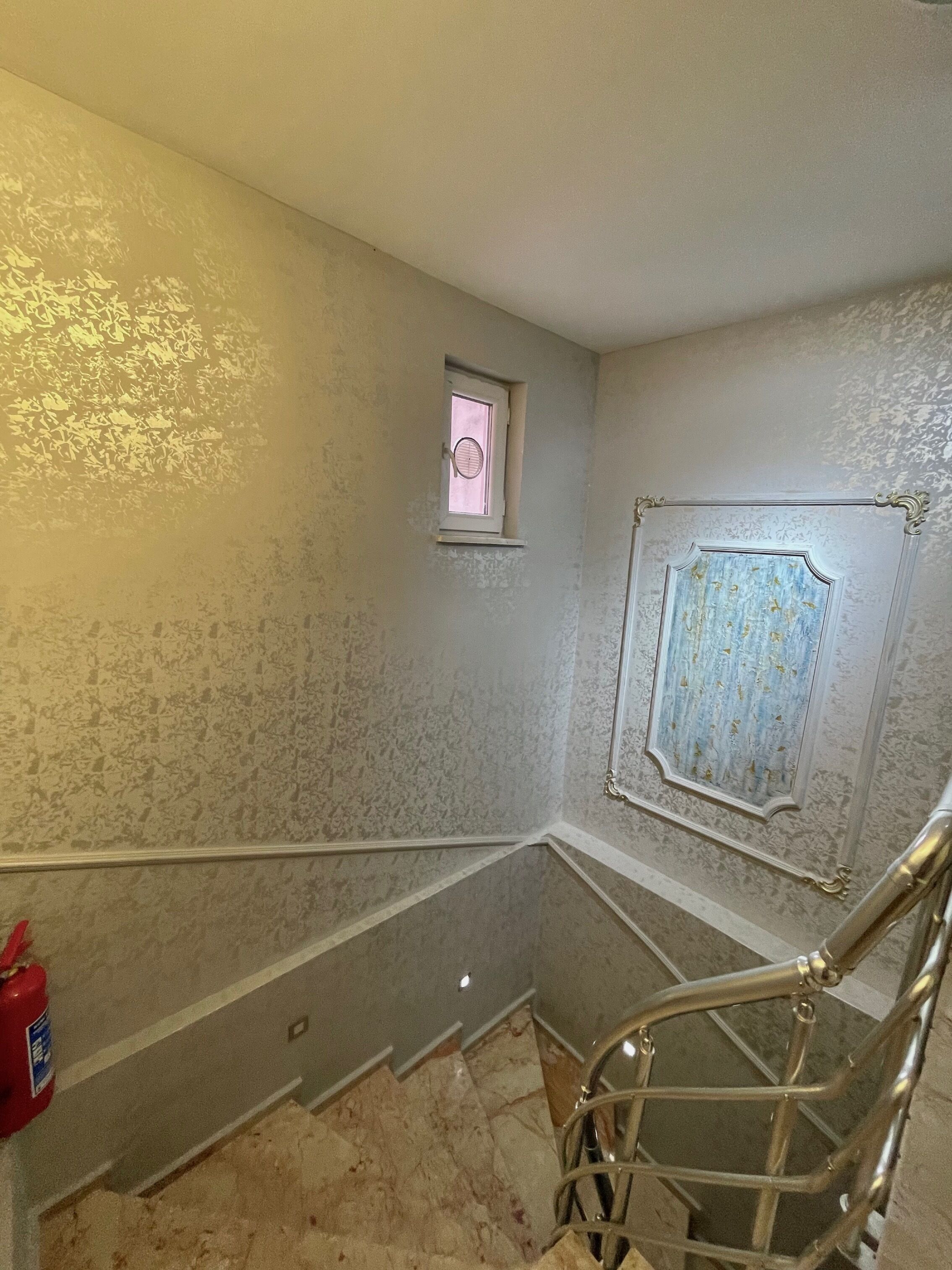 Una habitación con piso de mármol, un ventanal pequeño y una puerta con molduras decorativas.