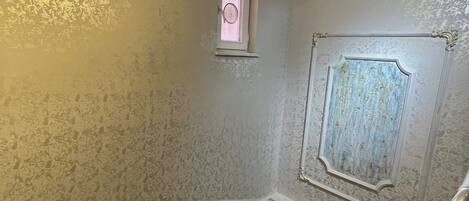 Una habitación con piso de mármol, un ventanal pequeño y una puerta con molduras decorativas.