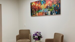 A modern room with two beige armchairs, a small table with a vase of flowers, and a colorful abstract painting on the wall. - Tekinler Otel (Balikesir)