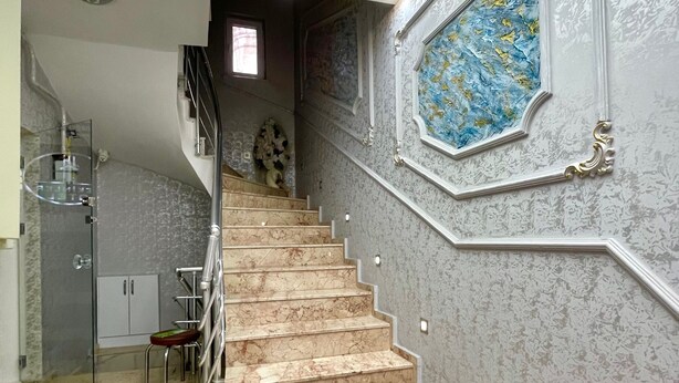 A marble staircase with a glass enclosure on the left, a decorative wall with a blue and gold pattern on the right, and a skylight above. - Tekinler Otel (Balikesir)