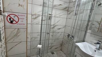 A bathroom with a glass shower enclosure, a toilet, and a sink.