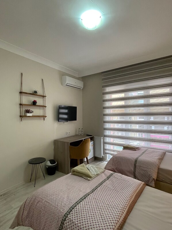 A hotel room with two beds, a desk, a TV, and a window with blinds. - Tekinler Otel (Balikesir)