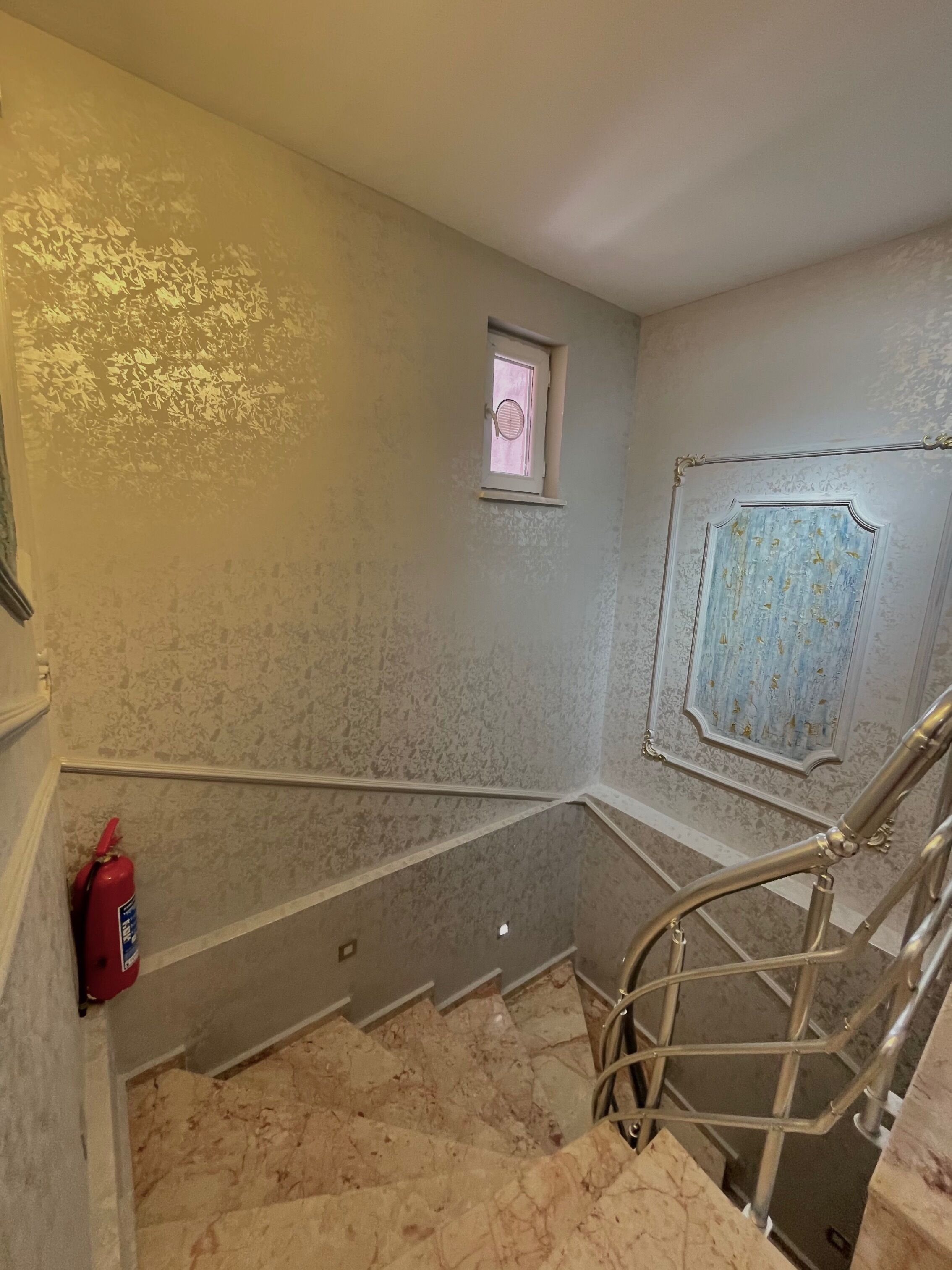 Una escalera con un extintor a la izquierda, un ventanal con una puerta y un panel decorativo en la pared.