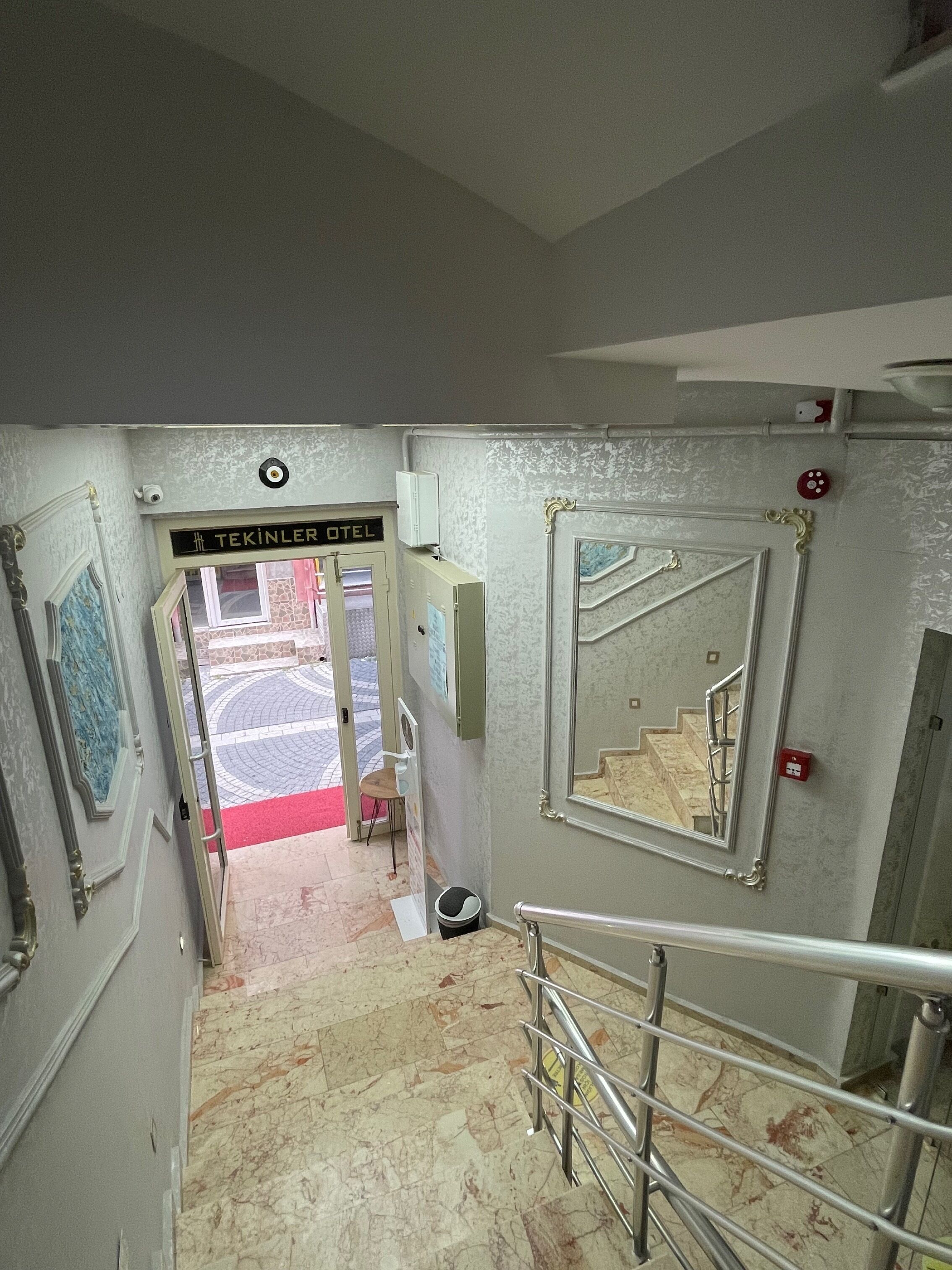 A hallway with a sign reading "TEKINLER OTEL" leading to a door, a mirror on the wall, and a staircase.