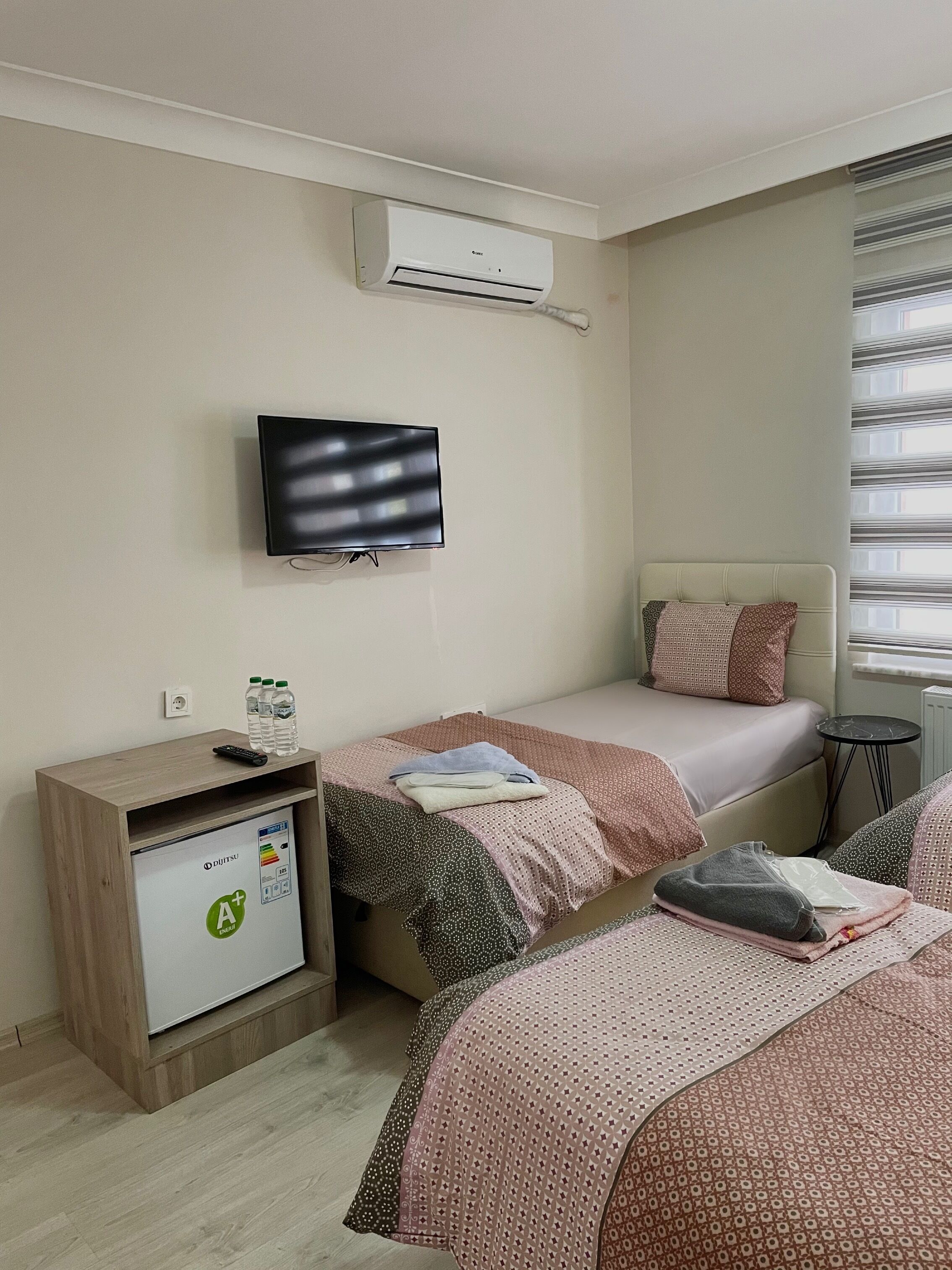 Habitación de hotel con dos camas, televisión, minibar y ventana con persianas.