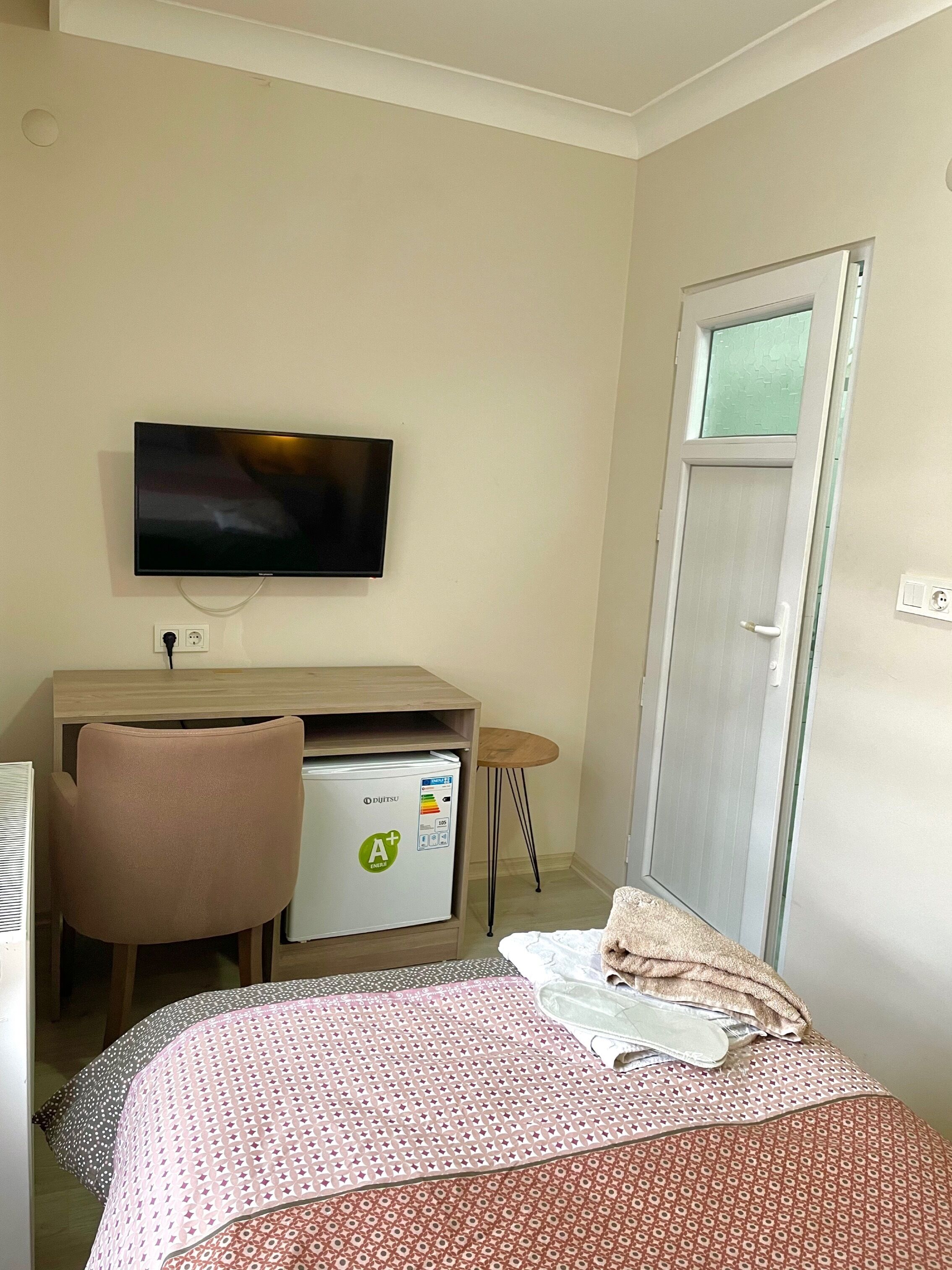 Ein Hotelzimmer mit einem Bett, einem Schreibtisch mit Computer, einem Sessel, einem Fernseher und einer Minibar.