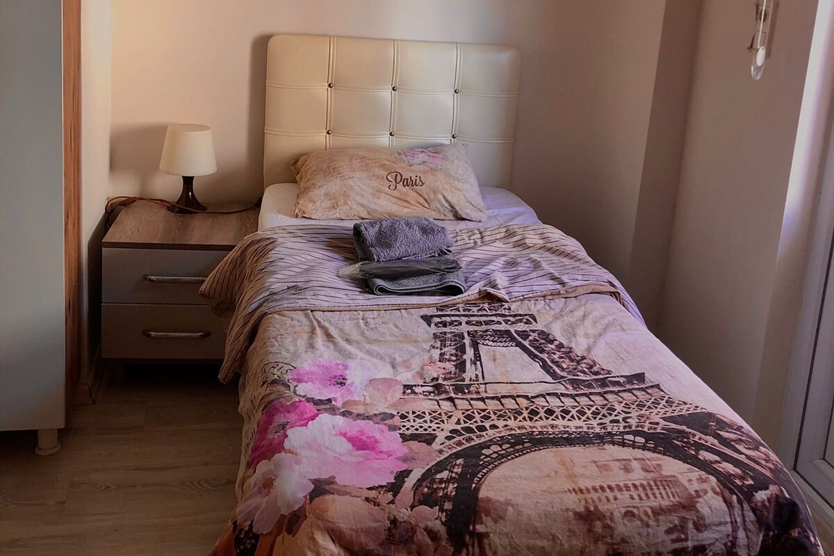 Un dormitorio con cama, mesita de noche, lámpara, aire acondicionado e iluminación en la pared.