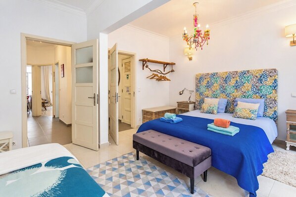 A bedroom with a large bed, a bench, a bedside table, a hanging light fixture, and a patterned headboard.