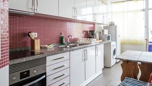 A modern kitchen with white cabinets, a red-tiled backsplash, stainless steel appliances, and a dining area with a table and chairs. - 1-Bedroom Flat with Terrace, near Metro and Arena (Loures)