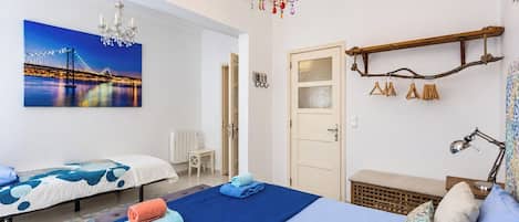 A hotel room with two beds, a large painting of a bridge, a chandelier, and a wooden shelf with hangers.
