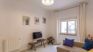 A living room with a TV, a small table, a sofa, and a window with curtains. - 1-Bedroom Flat with Terrace, near Metro and Arena (Loures)