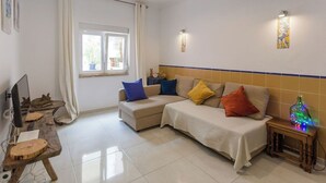 A living room with a sofa set, a TV, a wooden table, and a small side table with a decorative item. - 1-Bedroom Flat with Terrace, near Metro and Arena (Loures)