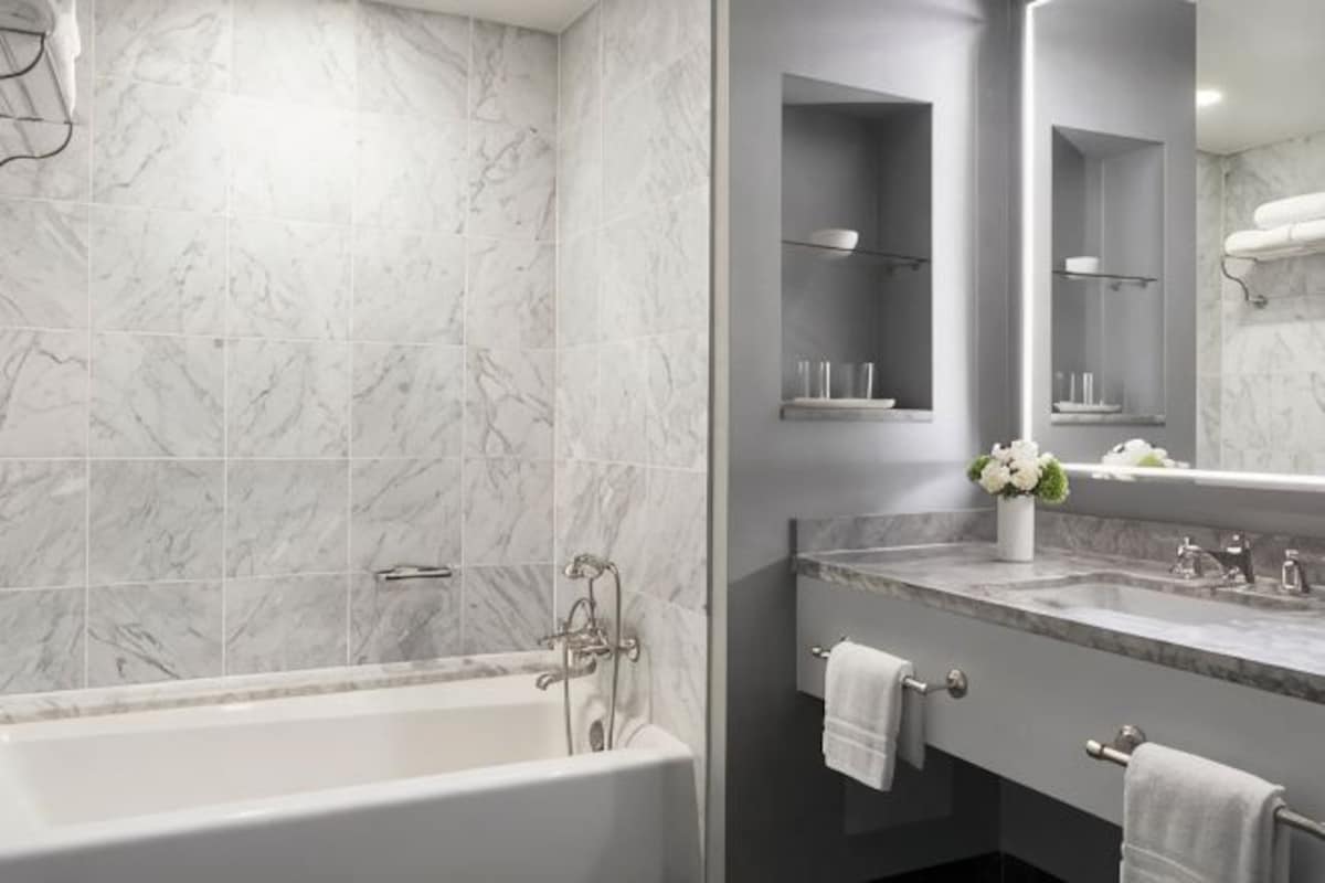 Un baño con bañera, tocador con espejo y repisa con artículos de aseo.
