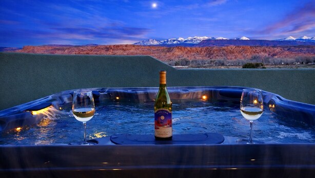 A hot tub with two glasses of wine and a bottle of wine, set against a mountainous backdrop at dusk. - Luxury Dual-Home Escape with 2 Hot Tubs, Bocce Court & Panoramic Red Rock Views (Moab)