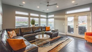 A spacious living room with a leather sofa, a round coffee table, and a view of a mountainous landscape through large windows. - Luxury Dual-Home Escape with 2 Hot Tubs, Bocce Court & Panoramic Red Rock Views (Moab)