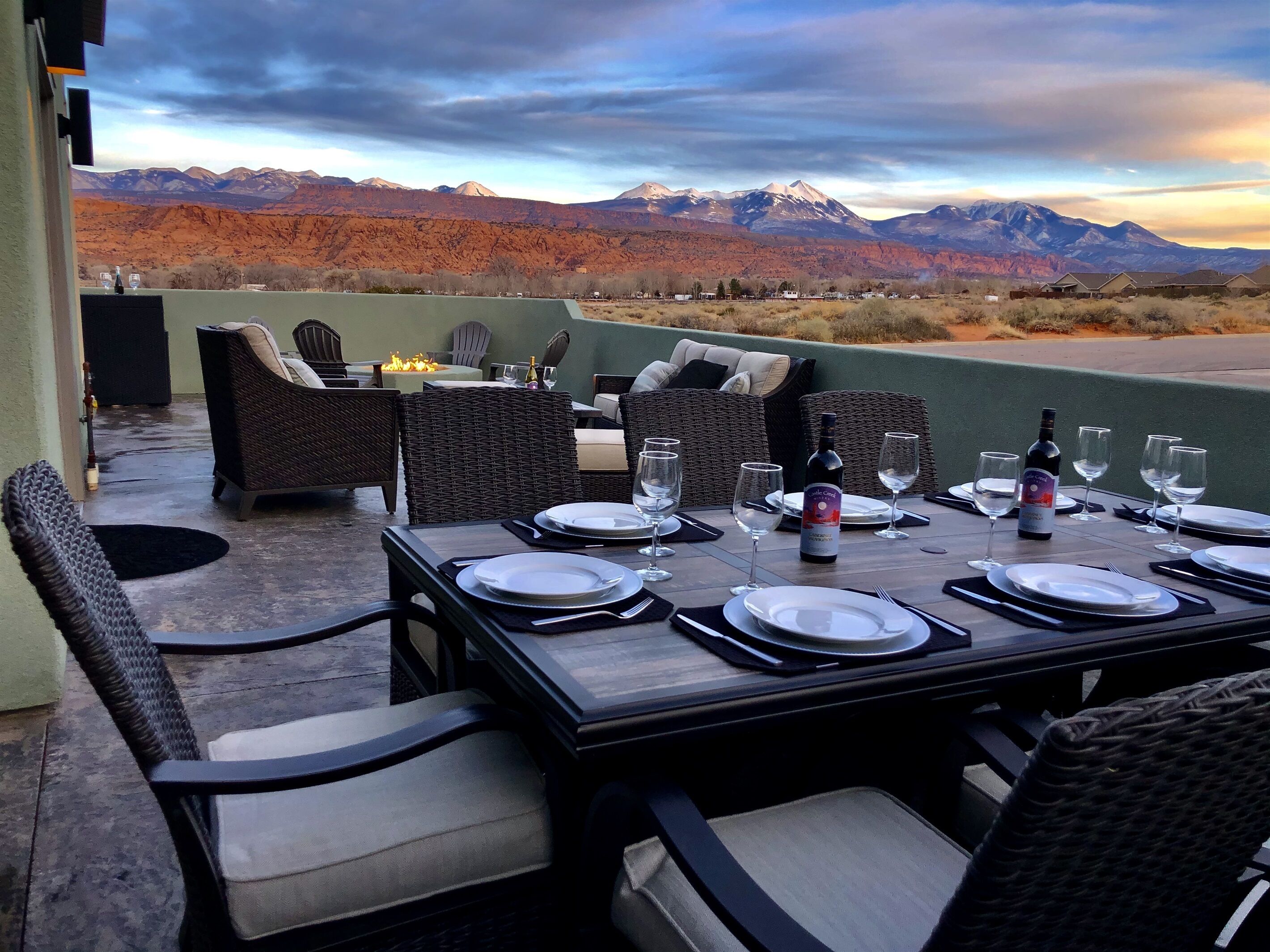 An outdoor dining area with a mountain view, wicker furniture, and a table set for four.