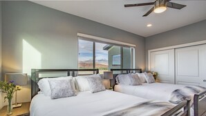 A bedroom with two beds, a ceiling fan, a window with a mountain view, and a door. - Luxury Dual-Home Escape with 2 Hot Tubs, Bocce Court & Panoramic Red Rock Views (Moab)