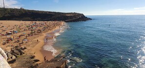 A beach with people, umbrellas, and rocky terrain.