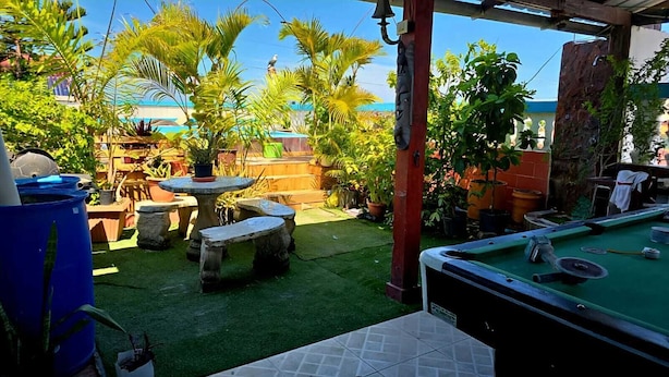 A pool table in a backyard with artificial grass, surrounded by potted plants and a wooden deck. - Hotel Kevin (Puerto Plata)