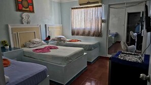 A hotel room with two single beds, a small table with a fan, a TV, and a window with curtains. - Hotel Kevin (Puerto Plata)