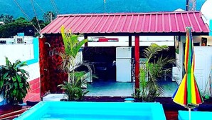 A pool area with a red-roofed structure, a blue pool, and a mountain in the background. - Hotel Kevin (Puerto Plata)