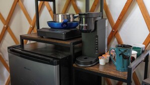 Een kitchenette met een koelkast, koffiezetapparaat en een klein tafeltje met bekers en een mandje.