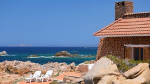 Ein Steinhaus mit Ziegeldach mit Blick auf eine zerklüftete Küstenlinie und das Meer.