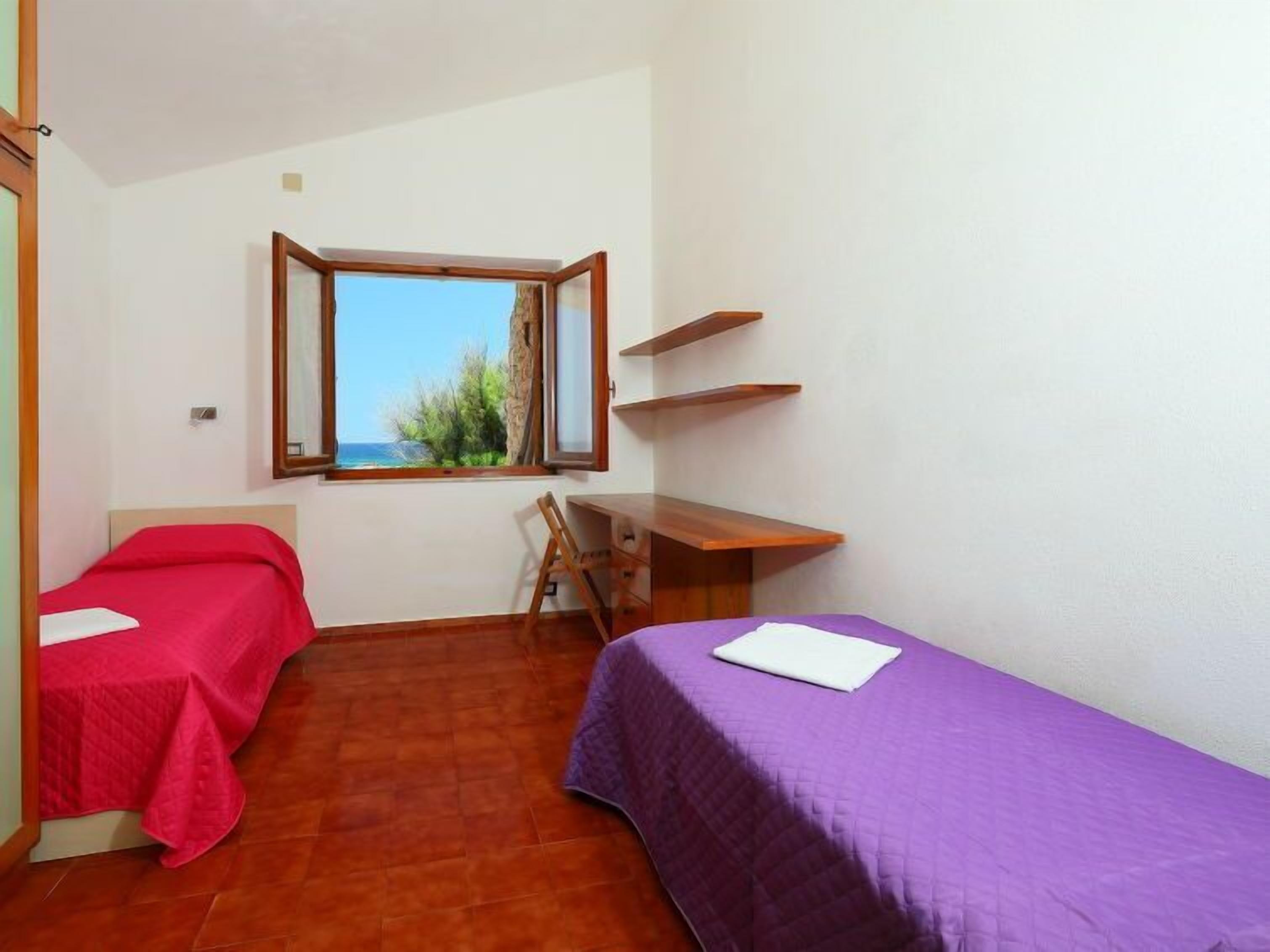 A small room with two beds, a desk, and a window with a view.