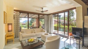 Amplia sala de estar con sofá, sillón y mesa de centro, ventanas grandes con vistas al exterior y ventilador de techo.
