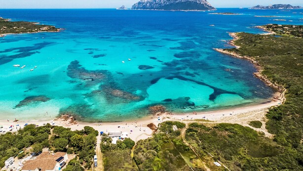 Una zona costera con aguas turquesas cristalinas, una playa arenosa y una isla rocosa distante.