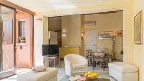 Una sala de estar moderna con una mesa de centro de vidrio, sofás blancos, un televisor y un comedor con una mesa y sillas.