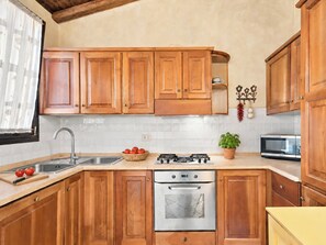 A kitchen with wooden cabinets, a stainless steel sink, a gas stove, an oven, and a microwave. - Vacation home Dalila by Interhome (Porto Istana)