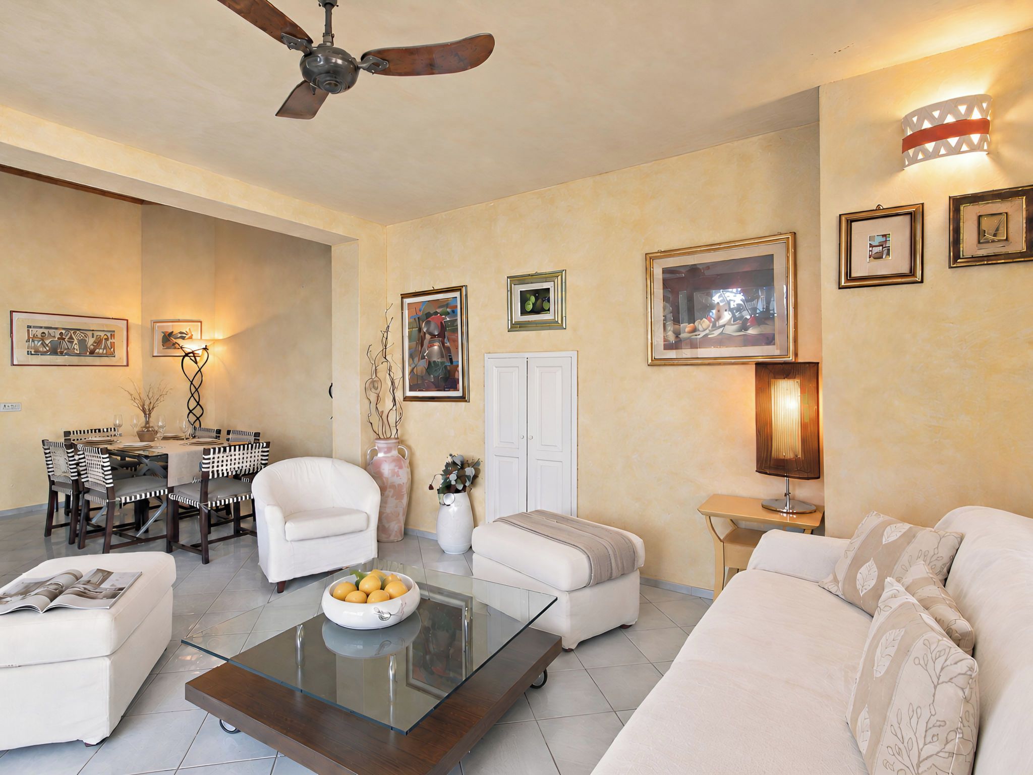 Un salon avec un ventilateur de plafond, un coin repas avec une table et des chaises, et un canapé.