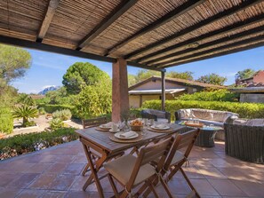 An outdoor patio with a table set for dining, surrounded by wicker furniture and a pergola overhead.