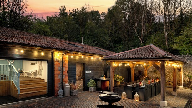 A brick patio with a fire pit, outdoor seating, and string lights. - Webbington Farm Holiday Cottages (Axbridge)