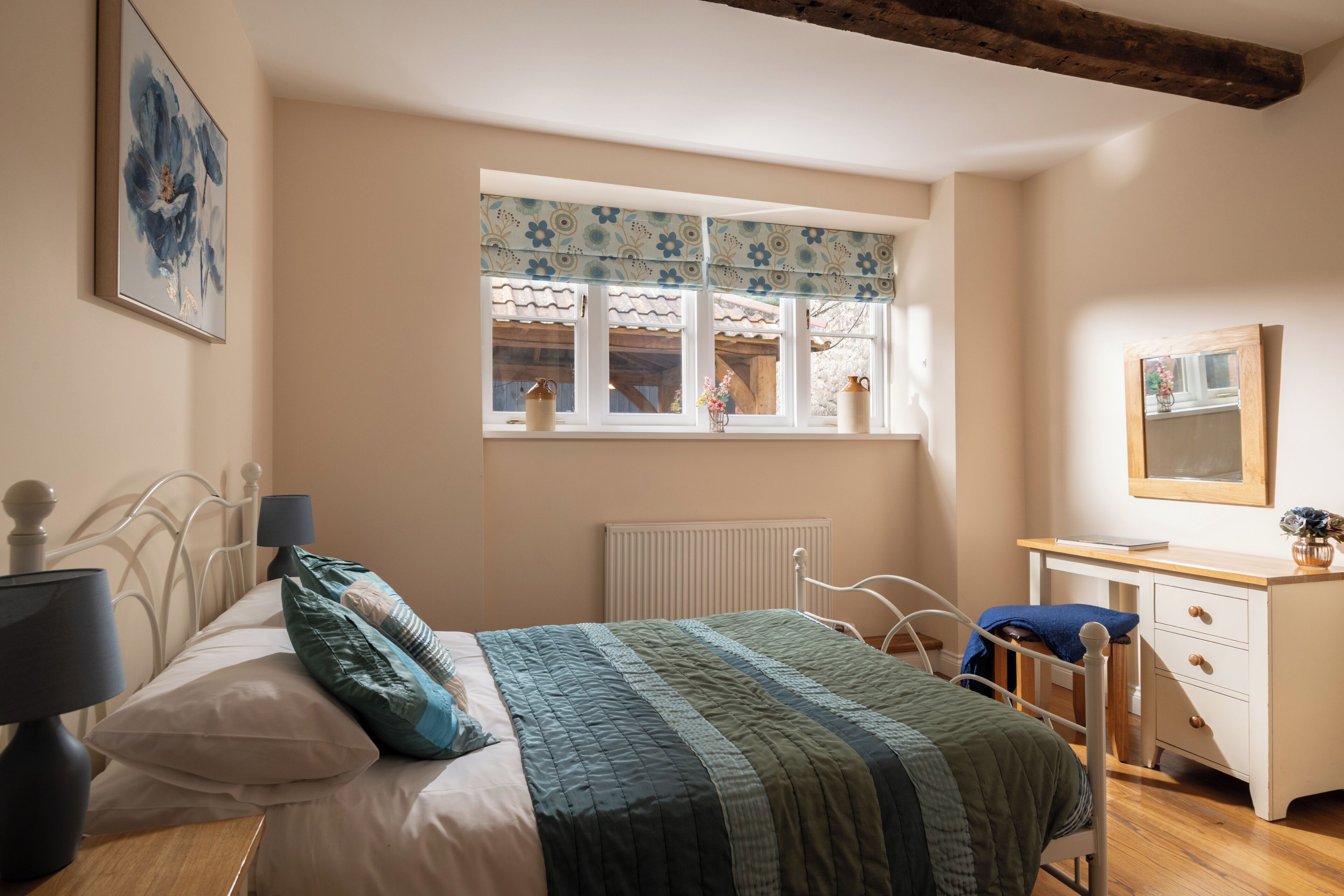 A bedroom with a bed, bedside table, dresser, and a window with curtains.