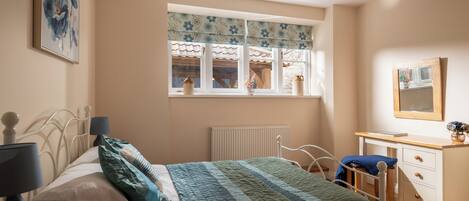 A bedroom with a bed, bedside table, dresser, and a window with curtains.