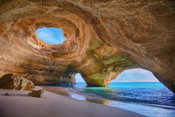 Experience the serene beauty of a natural rock formation, situated on a sandy beach, leading to a calm sea.